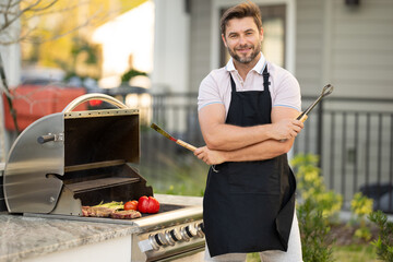 Male chef grilling and barbequing in garden. Barbecue outdoor garden party. Handsome man preparing barbecue meat. Concept of eating and cooking outdoor during summer time.