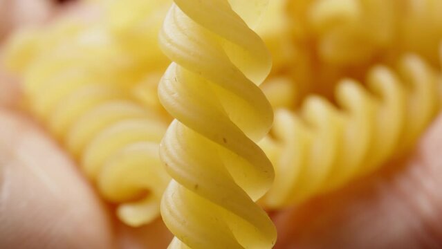A single fusilli pasta rotates on a black background while I pour other pasta from the palm of my hand. close-up
