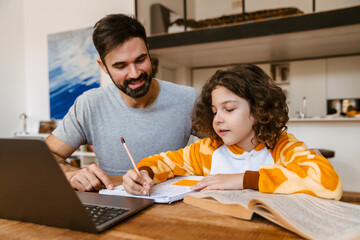 Father helping his son with homework while sitting with laptop at table