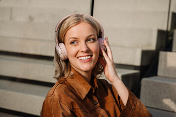 Portrait of smiling woman listening music with headphones while sitting on stairs outdoors