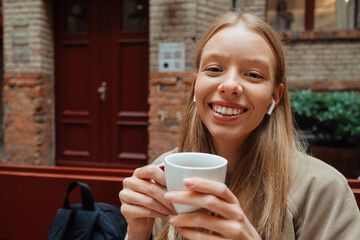 Smiling woman drinking coffee while sitting in cafe outdoors