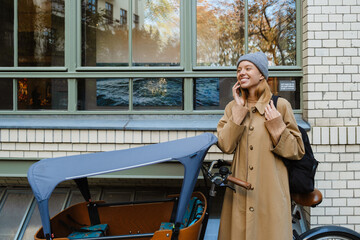 Cheerful girl talking on cellphone while standing with bike outdoors