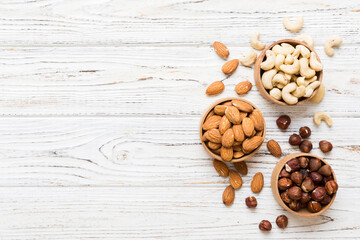 Assortment of nuts in wooden bowl on colored table. Cashew, hazelnuts, walnuts, almonds. Mix of nuts Top view with copy space