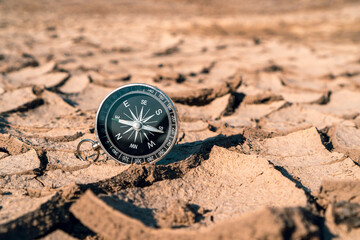 Fototapeta na wymiar Black compass on the dried and cracked earth background