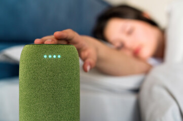 A sleeping woman turning off alarm clock on a portable wireless speaker