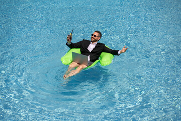 Successful business man floating in suit in pool water. Summer vacations and travel concept. Funny business man drink summer cocktail and using laptop in swimming pool. Summer business concept.