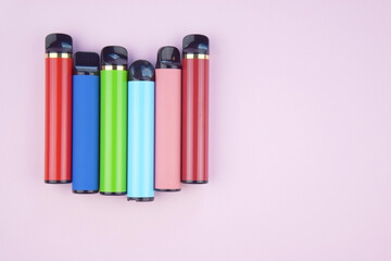 Set of multicolor disposable electronic cigarettes on a pink background.