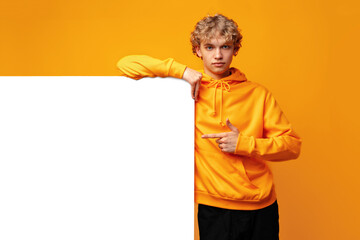 Young man holding a blank panel for advertising against yellow background