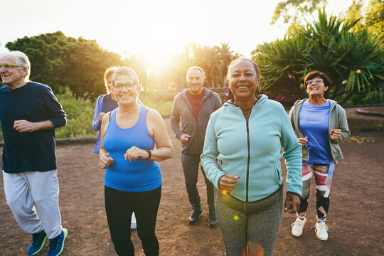Fit senior people running at city park - Group of elderly friends doing sport workout together outdoor - Main focus on african woman face