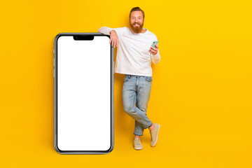 Full length photo of beard man near hold telephone wear shirt jeans shoes isolated on yellow color background