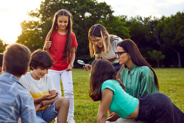 School children together with teacher have fun on field trip. Group of happy excited kids enjoying interesting lesson, learning about world of insects, searching for bugs, exploring wonders of nature
