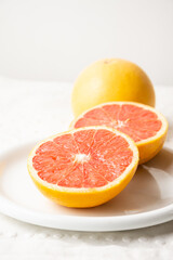 Naklejka na ściany i meble View of split red grapefruit with one whole on plate and white tablecloth, white background, vertical