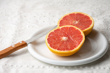 Top view of split red grapefruit on plate, white tablecloth and knife, horizontal, with copy space