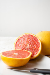Close-up of split red grapefruit with one whole on plate and white background, vertical, with copy space