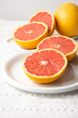 Fototapeta na wymiar Top view of split red grapefruits on plate and white tablecloth, vertically, with copy space