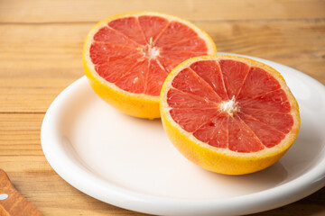 Naklejka na ściany i meble Close-up of split red grapefruit on white plate on wooden table, horizontal, with copy space