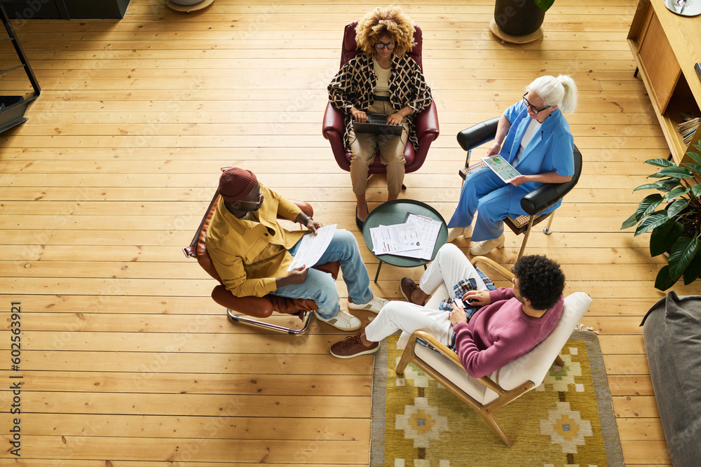 Poster above view of four intercultural brokers in smart casualwear having discussion of papers or working 