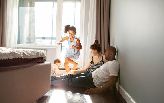 Snapshot of diverse family playing with happy children on floor at home run around in motion, authentic family life, unposed, spontaneous moments of fun and laughter