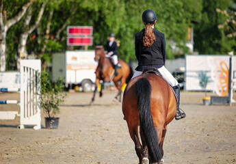 Rider with horse from behind in a show jumping tournament, out of focus in the background another...