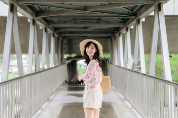 Obraz premium young asian woman traveler with weaving basket using mobile phone and standing on overpass. Journey trip lifestyle, world travel explorer or Asia summer tourism concept.