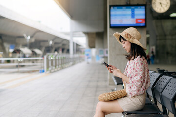 young asian woman traveler with weaving basket using a mobile phone and waiting for train in train station. Journey trip lifestyle, world travel explorer or Asia summer tourism concept.