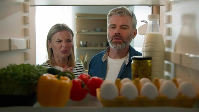 POV Point of view from inside fridge adult couple feeling bad disgusting unpleasant smell from broken refrigerator spoiled rotten food meal middle-aged man and woman awful smelling stink from freezer