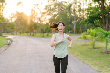 Fit Asian young woman jogging in park smiling happy running and enjoying a healthy outdoor lifestyle. Female jogger. Fitness runner girl in public park. healthy lifestyle and wellness being concept