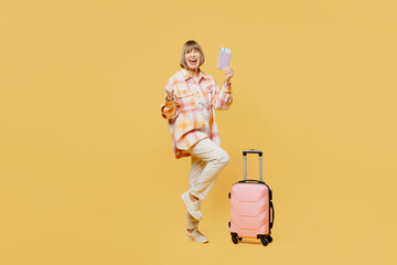 Full body traveler woman 50 years old wear casual clothes hold bag passport ticket isolated on plain yellow background. Tourist travel abroad in free spare time rest getaway. Air flight trip concept.