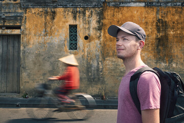 Portrait of traveler with backpack. Man exploring streets of ancient city Hoi An in Vietnam..