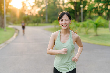 Fit Asian young woman jogging in park smiling happy running and enjoying a healthy outdoor lifestyle. Female jogger. Fitness runner girl in public park. healthy lifestyle and wellness being concept
