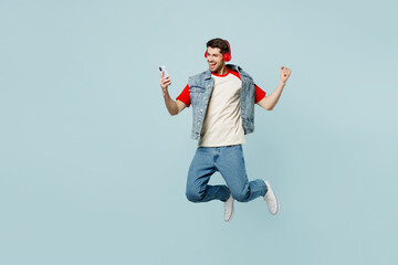 Full body young man wear denim vest red t-shirt casual clothes jump high listen music in headphones...