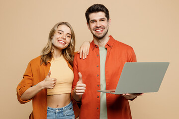 Young fun couple two friends family IT man woman wear casual clothes hold use work on laptop pc computer together show thumb up isolated on pastel plain light beige color background studio portrait.