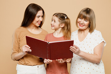 Happy smiling adorable fun women wear casual clothes with child kid girl 6-7 years old. Granny mother daughter read look at photo album isolated on plain beige background. Family parent day concept.