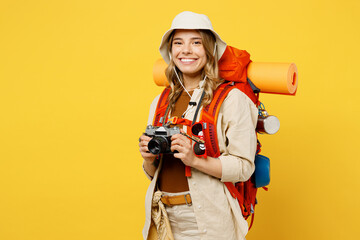 Young happy woman carry backpack with stuff mat hold in hand photo camera isolated on plain yellow background. Tourist leads active lifestyle walk on spare time. Hiking trek rest travel trip concept.