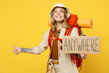 Young fun woman carry backpack with stuff mat holding card sign anywhere do hitch-hiking gesture isolated on plain yellow background. Tourist walk on spare time. Hiking trek rest travel trip concept. - obrazy, fototapety, plakaty