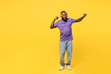 Fototapeta na wymiar Full body young man of African American ethnicity he wears casual clothes purple t-shirt headphones listen to music raise up hands dance isolated on plain yellow background studio. Lifestyle concept.