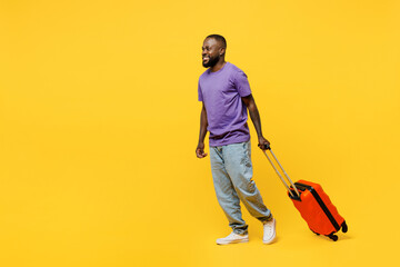 Traveler man wears casual clothes t-shirt hold suitcase go isolated on plain yellow background studio portrait. Tourist travel abroad in free spare time rest getaway. Air flight trip journey concept.