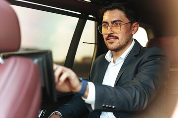 Young elegant businessman watching TV on the screen in luxury car