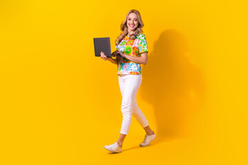 Full length photo of pretty girl dressed colorful t-shirt white trousers hold laptop walk empty space isolated on yellow color background