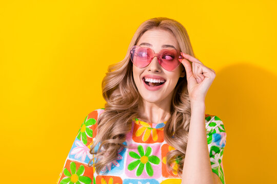Photo of pretty lady try on sunglass watch side low price shop store poster wear flower print shirt isolated yellow color background