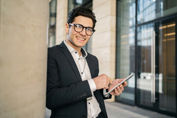 An entrepreneur, a creative director, a young male businessman in formal clothes, stands near the office and uses a tablet.
