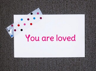 White note stick on dark background with handwritten text YOU ARE LOVED, positive affirmation to...