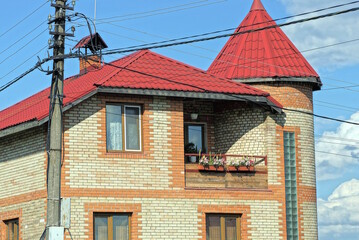 brown attic of a private house with a window and an open balcony under a red tiled roof on the street against a blue sky