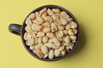 gray brown peanuts in a ceramic cup on a yellow table
