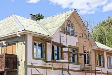 brown attic of a private house being repaired and insulated with white pinoblocks near scaffolding under a gray slate roof against a blue sky