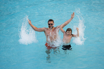 Father and son swimming in pool, summer family weekeng. Father and son splash water in pool on summer family holiday. Dad and child relaxing in pool water. Child with dad swimming in pool.