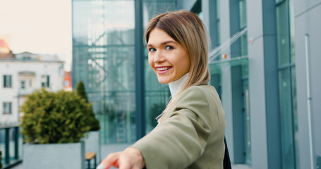 Back view of woman in classic suit confidently walking the streets of the urban city and showing follow me gesture on camera. Follow me concept.