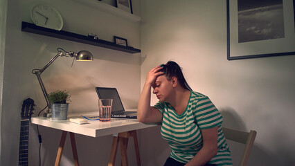 Woman with stomach and headache while working at home on a laptop.