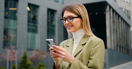 Portrait beautiful businesswoman wearing smart casual clothes using smartphone on urban street. Attractive girl holding mobile phone in hand outdoor.