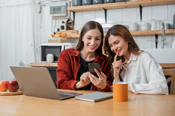 Fototapeta premium Two teenage girls are happy to receive messages from phone, social media in the kitchen